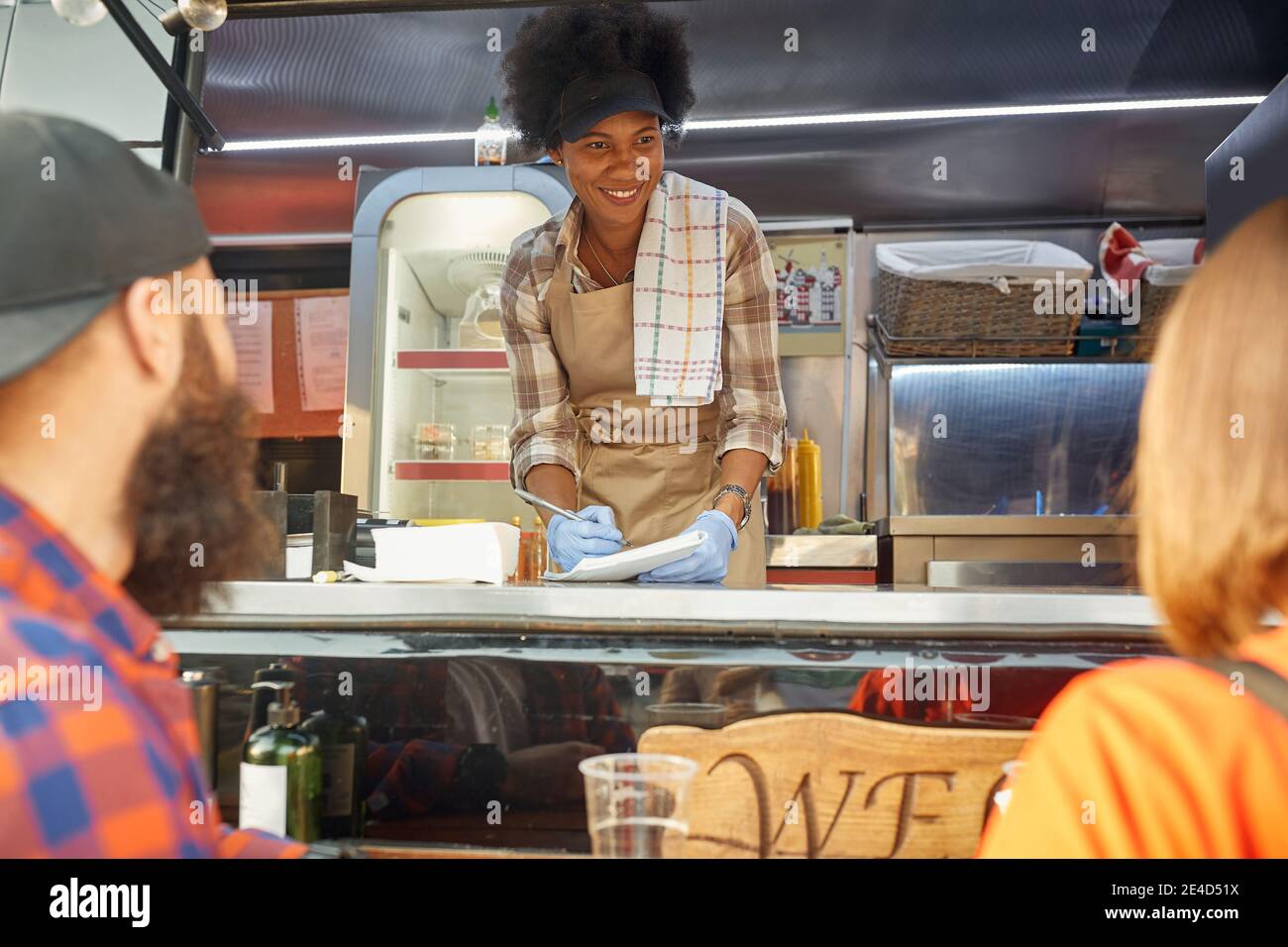 young urban couple ordering food to female afro-american employee in food-truck Stock Photo