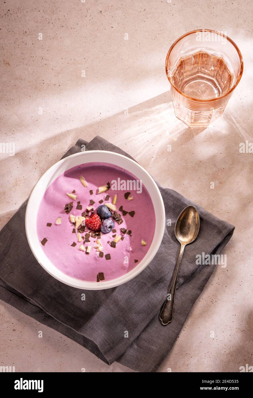 A simple summer dinner made of a big bowl of berries yoghourt with some chocolate and nuts as topping and a glass of water Stock Photo