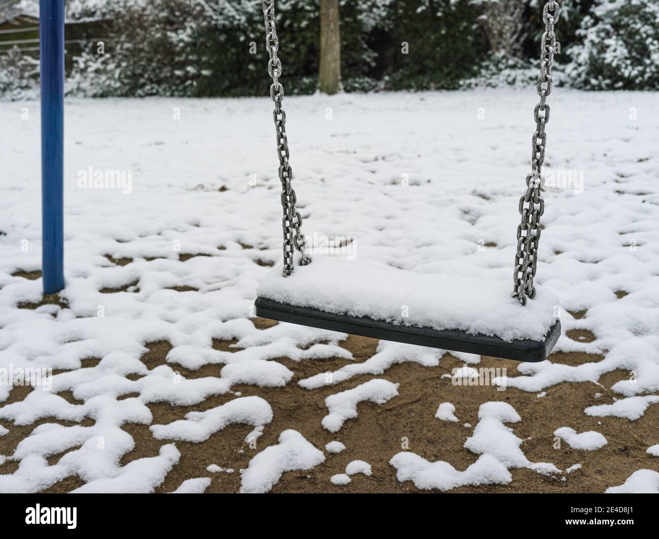 Snow-covered swing in an abandoned playground on a cloudy January morning. Stock Photo