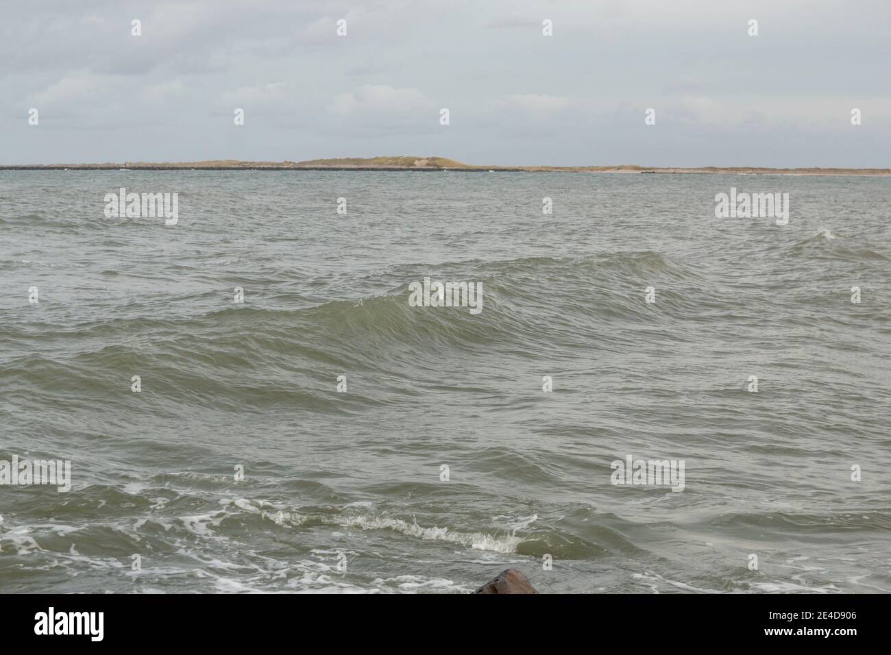 Coast line at Thyboron on the Danish west coast, clouds in the sky, waves in the sea, white foam splashes, rocks. Stock Photo