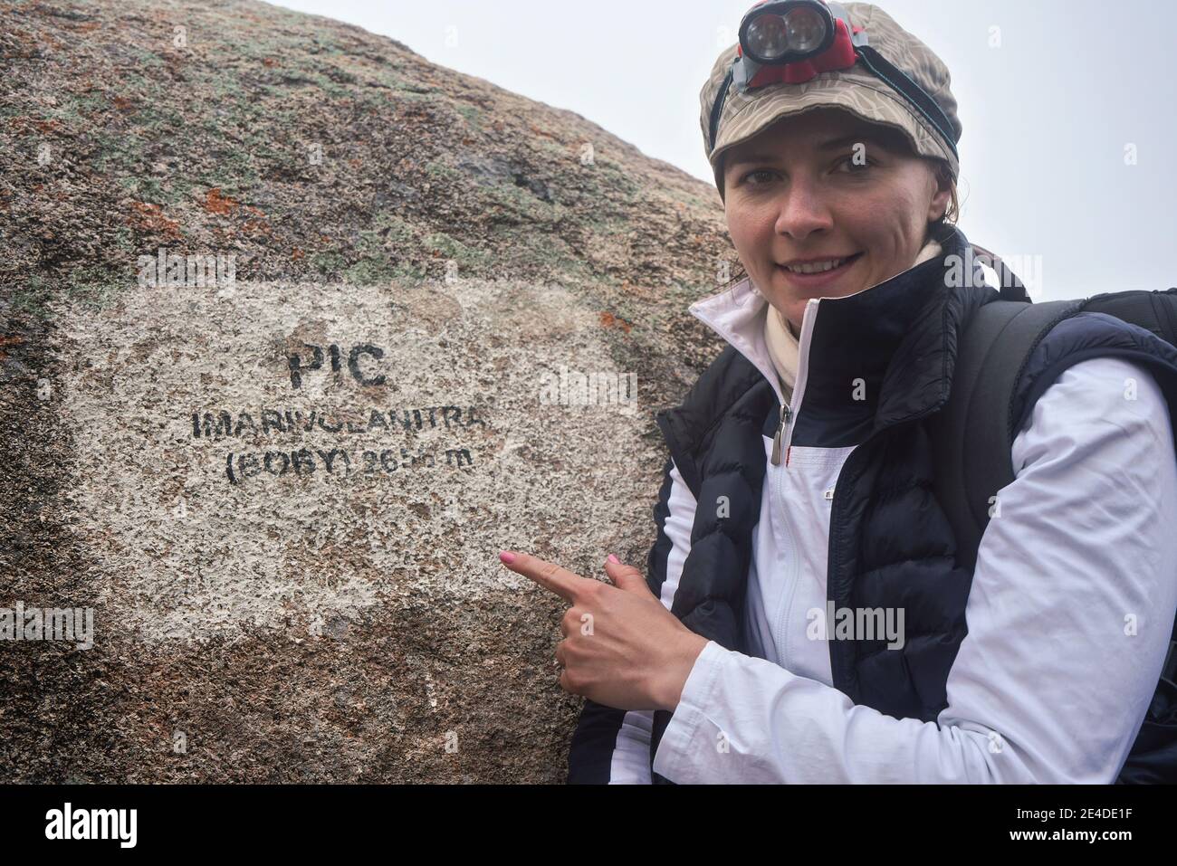 Young woman in warm jacket, lamp on head, pointing to sign at summit of Pic Boby (Imarivolanitra in local) peak - highest accessible point in Madagasc Stock Photo