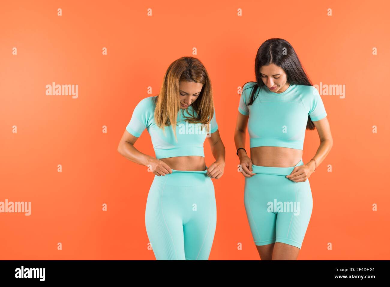 Young fit athletic women flexing their abs, wearing turquoise