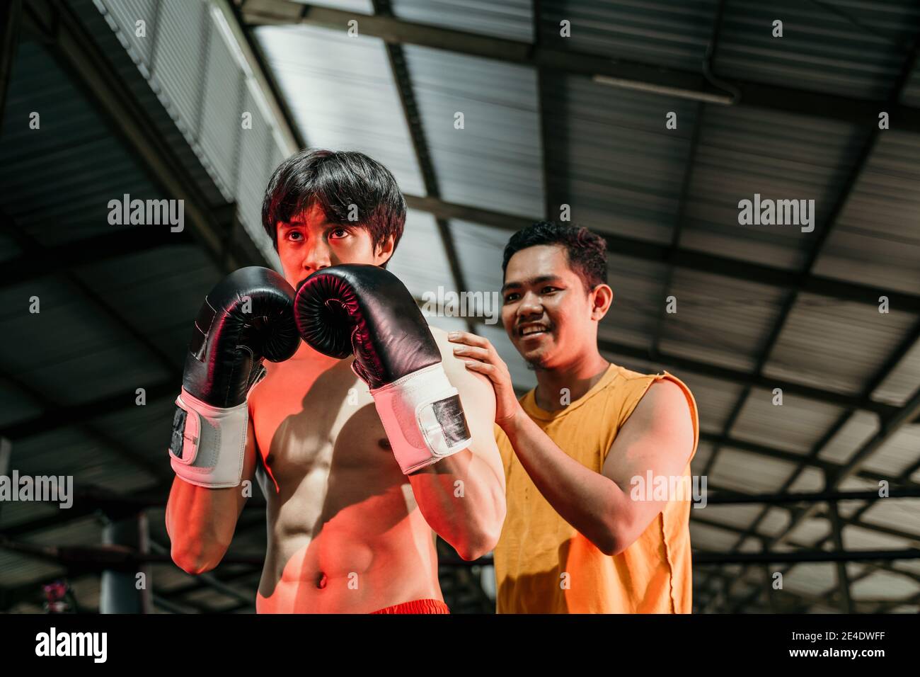 man wearing boxing gloves with her trainer standing on the boxing ring