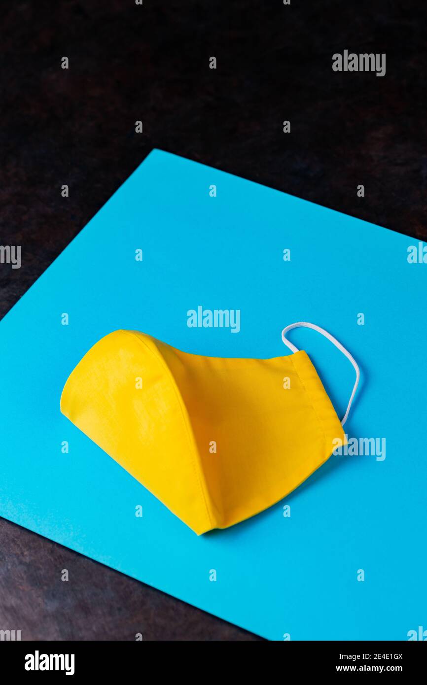 Yellow face mask on blue paper. Reusable protective mask. Face protective mask on a dark background. Pop art protective concept. Copy space Stock Photo