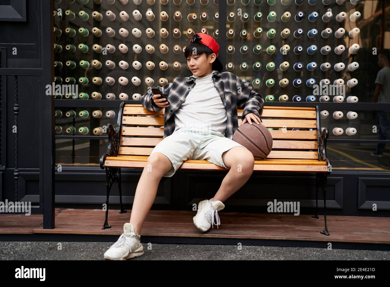 fifteen-year-old teenage asian boy sitting on bench looking at cellphone Stock Photo