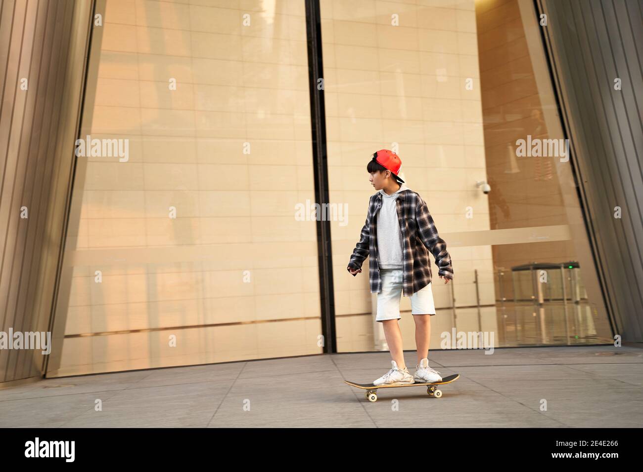 fifteen-year-old teenage asian boy skateboarding in front of modern building Stock Photo