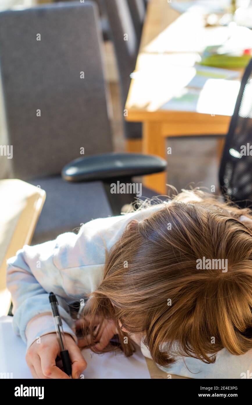 A girl writes out her school work on a piece of paper during a home school lesson Stock Photo