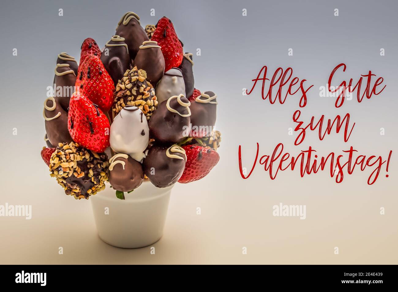 Happy valentine's day greeting card in German with red lettering that reads Alles Gute zum Valentinstag; Bunch of edible flowers, arrangement of choco Stock Photo