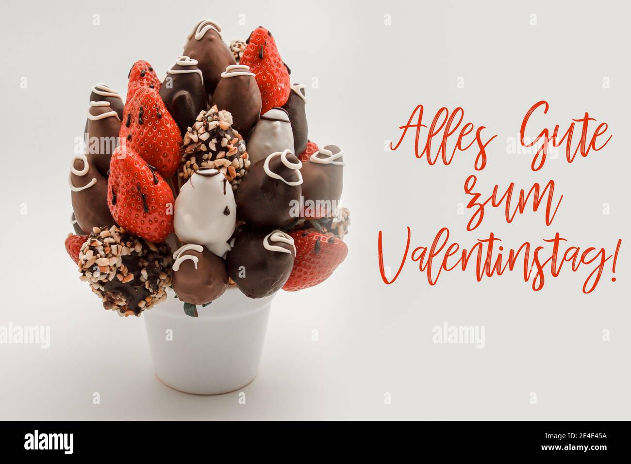 Happy valentine's day greeting card in German with red lettering that reads Alles Gute zum Valentinstag; Bunch of edible flowers, arrangement of choco Stock Photo