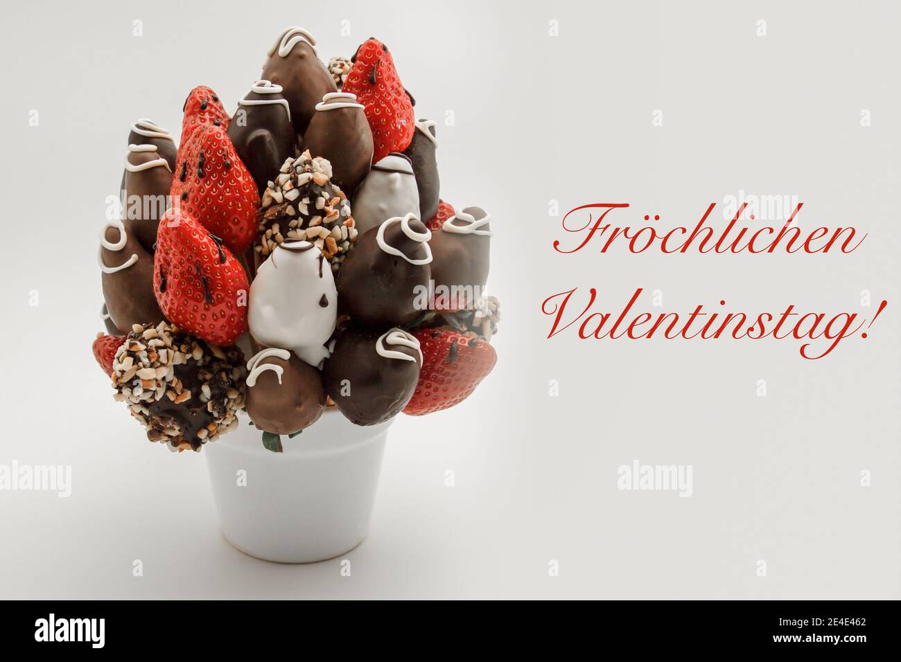 Happy valentine's day greeting card in German with red lettering that reads Fröchlichen Valentinstag; Bunch of edible flowers, arrangement of chocolat Stock Photo