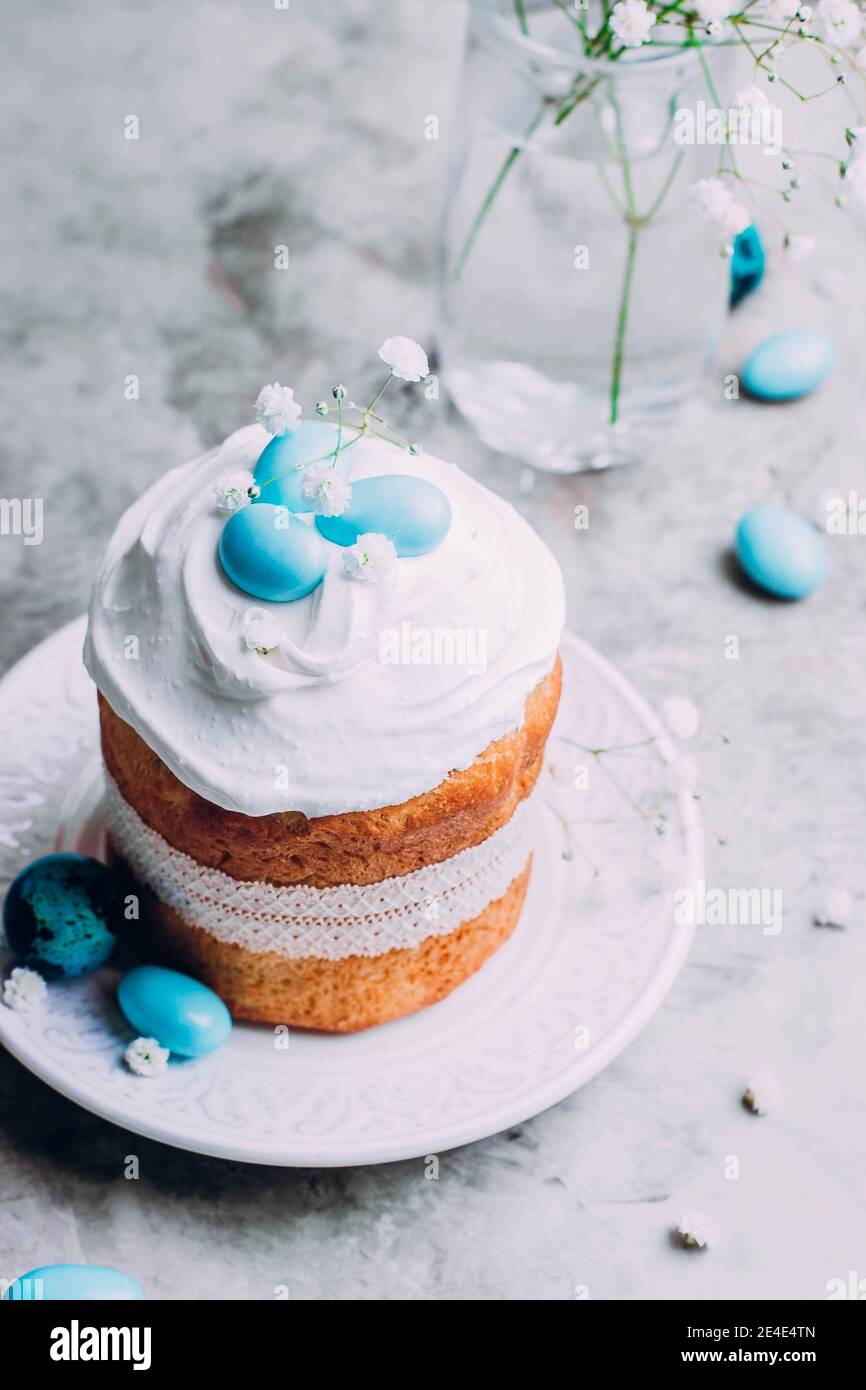 Easter cake kulich. Traditional Easter sweet bread decorated meringue and blue candy cane shape eggs on plate on gray stone table background. Copy spa Stock Photo