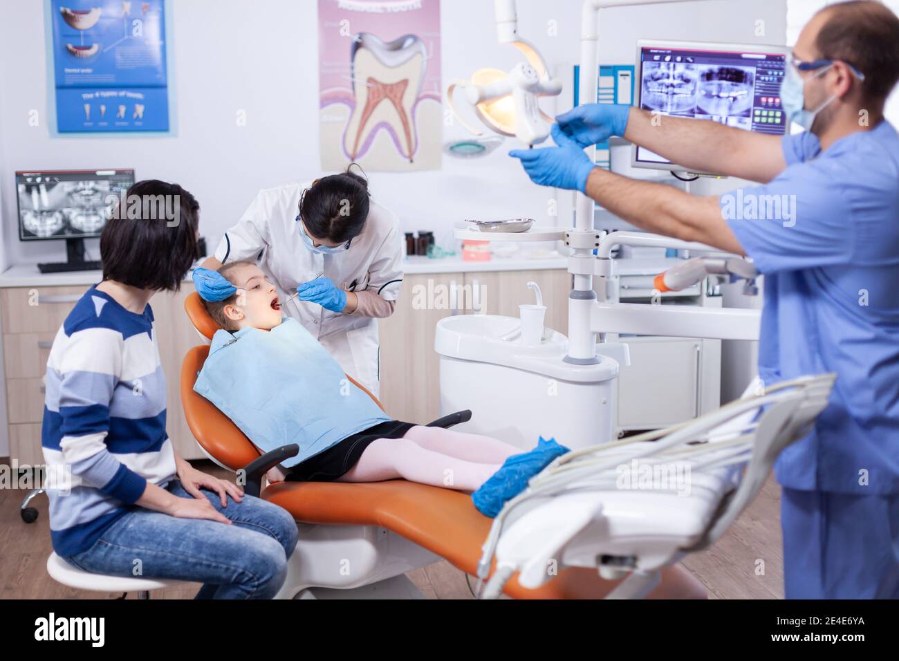 Kid patient in dental office getting teeth treatment sitting on dental  chair wearing bib with mouth open. Dentistry specialist during child cavity  consultation in stomatology office using modern technology Stock Photo -