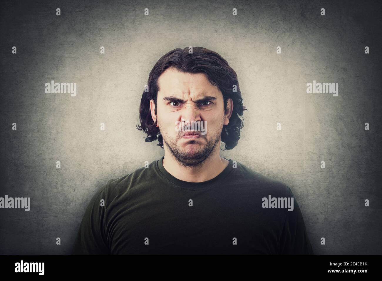 Bewildered and confused young man looking perplexed and upset to camera isolated on grey wall background. Angry casual guy, long curly hair style, irr Stock Photo