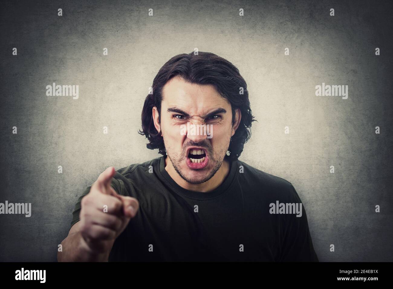 Furious young man pointing forefinger to camera blaming someone as guilty, or scolding isolated on grey wall background. Angry guy screaming and showi Stock Photo