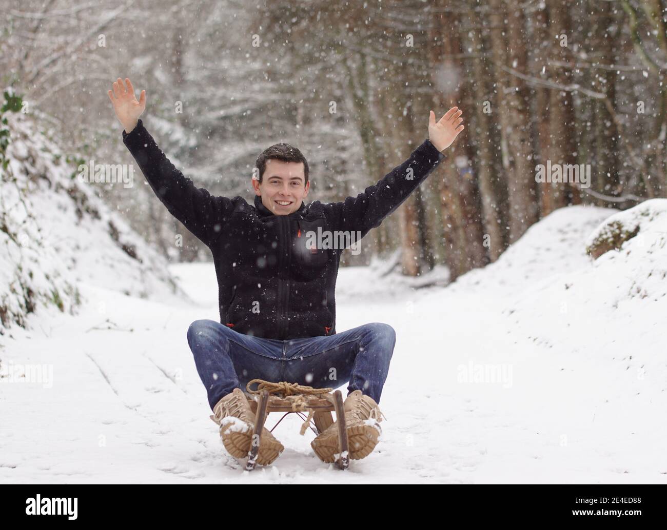 Winter time - Man riding a sledge putting the hands up and smiling Stock Photo
