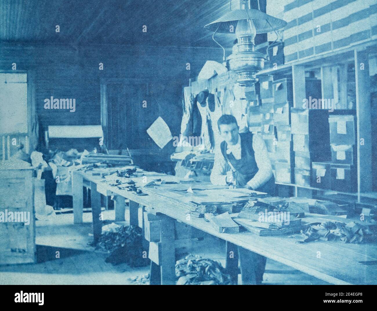 American archive cyanotype portrait of a man working at a workshop bench with a large oil lamp hanging from the ceiling. Taken in the late 19th century in Port Byron, NY, USA Stock Photo