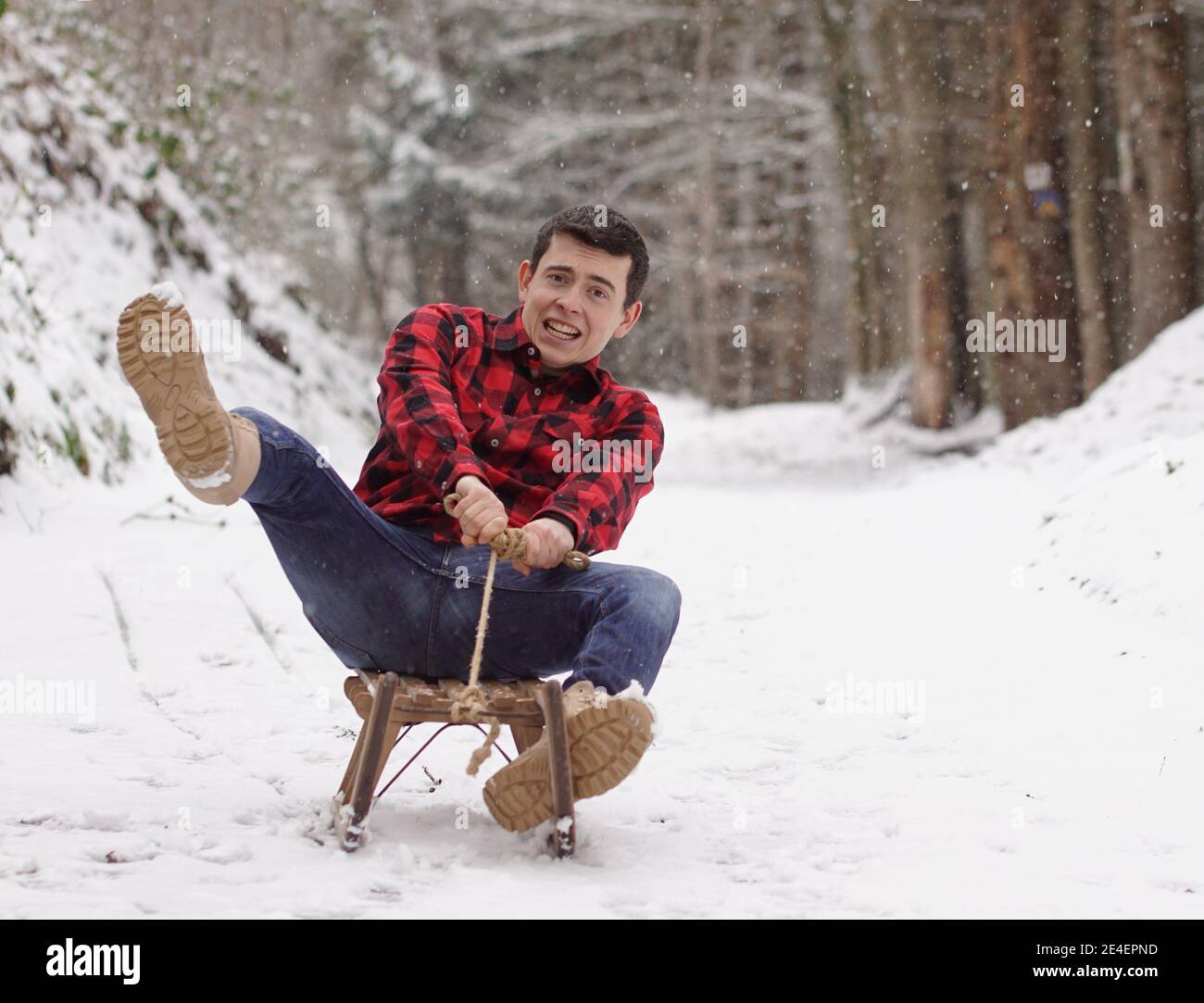 Man riding a sleigh with frightened and anxious face, fear of falling off the sledge - it's getting to fast Stock Photo