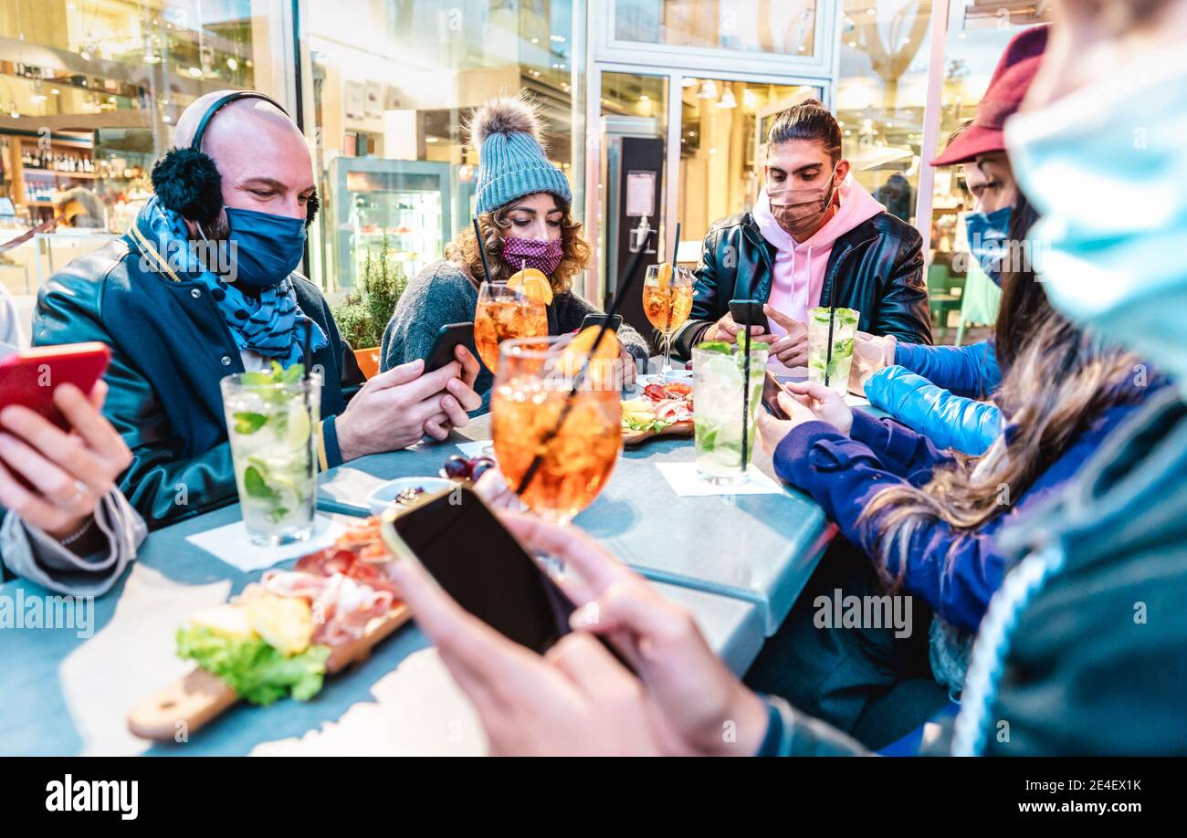 Millenial friends using mobile smart phones at cocktail bar - New normal lifestyle concept with people on contact tracing app during pandemic Stock Photo