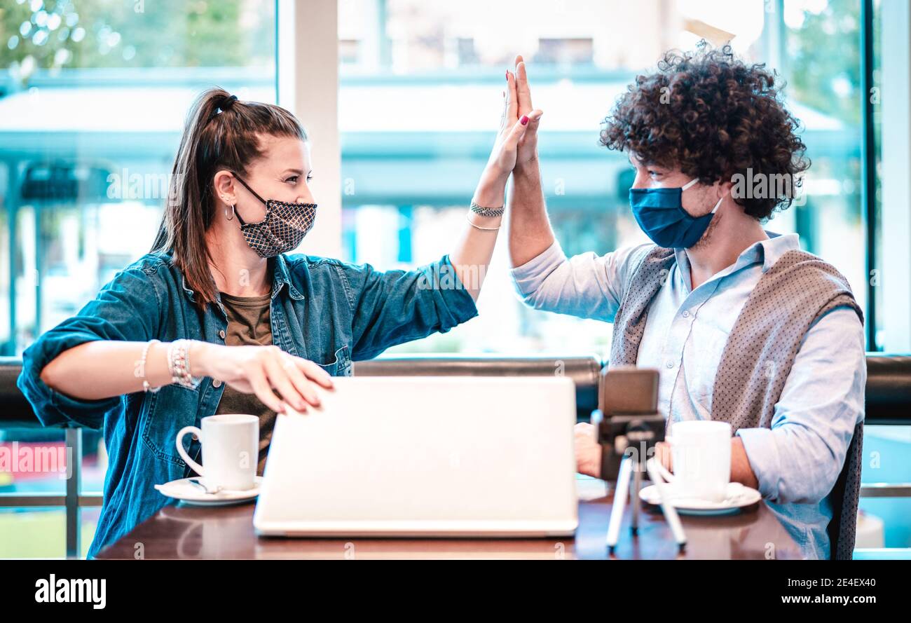 Young milenial influencers at coworking space with facemask - New normal marketing concept with next generation couple having fun Stock Photo