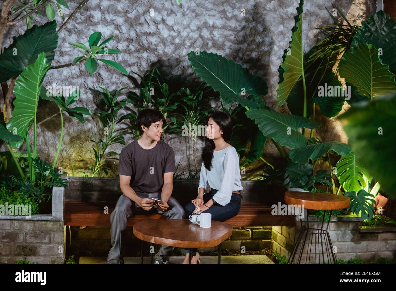 dating a couple of asian teenagers sitting on wooden benches in the garden of the house Stock Photo