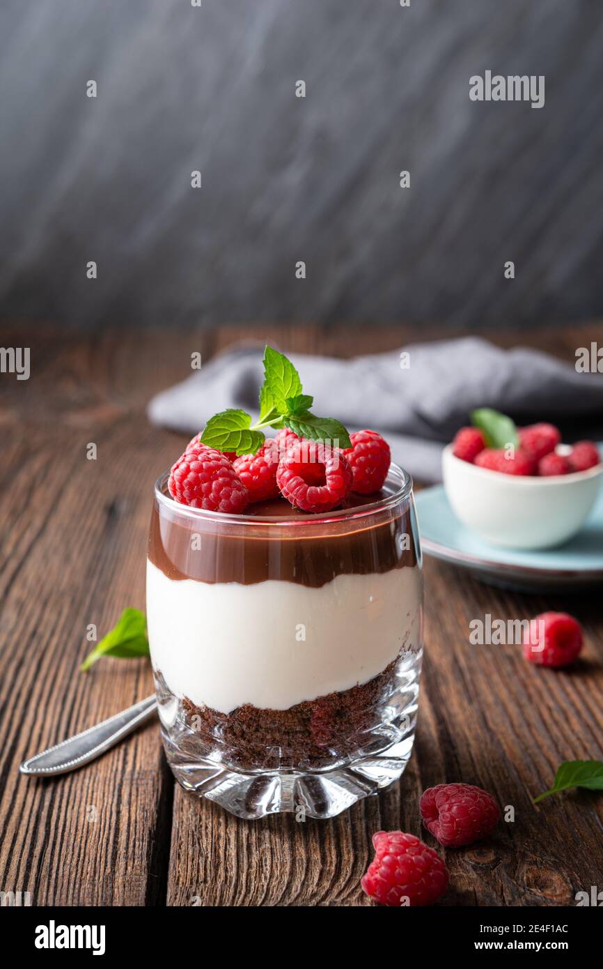 Delicious layered dessert with cream cheese, crushed chocolate cookies, topped with ganache and fresh raspberries in a jar Stock Photo