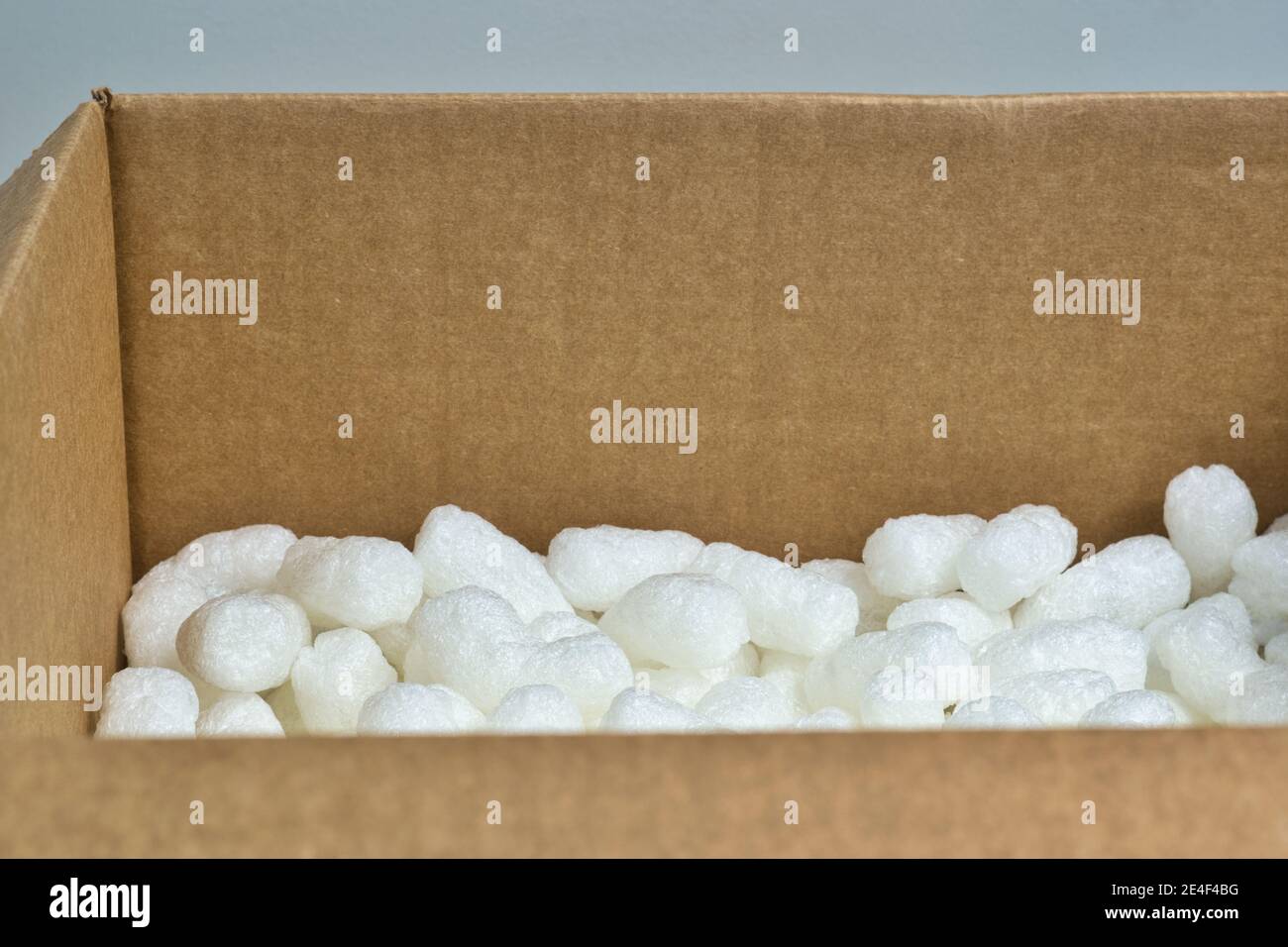 White packing peanuts styrofoam popcorn packaging material inside a cardboard box, angle view with copy space. Stock Photo