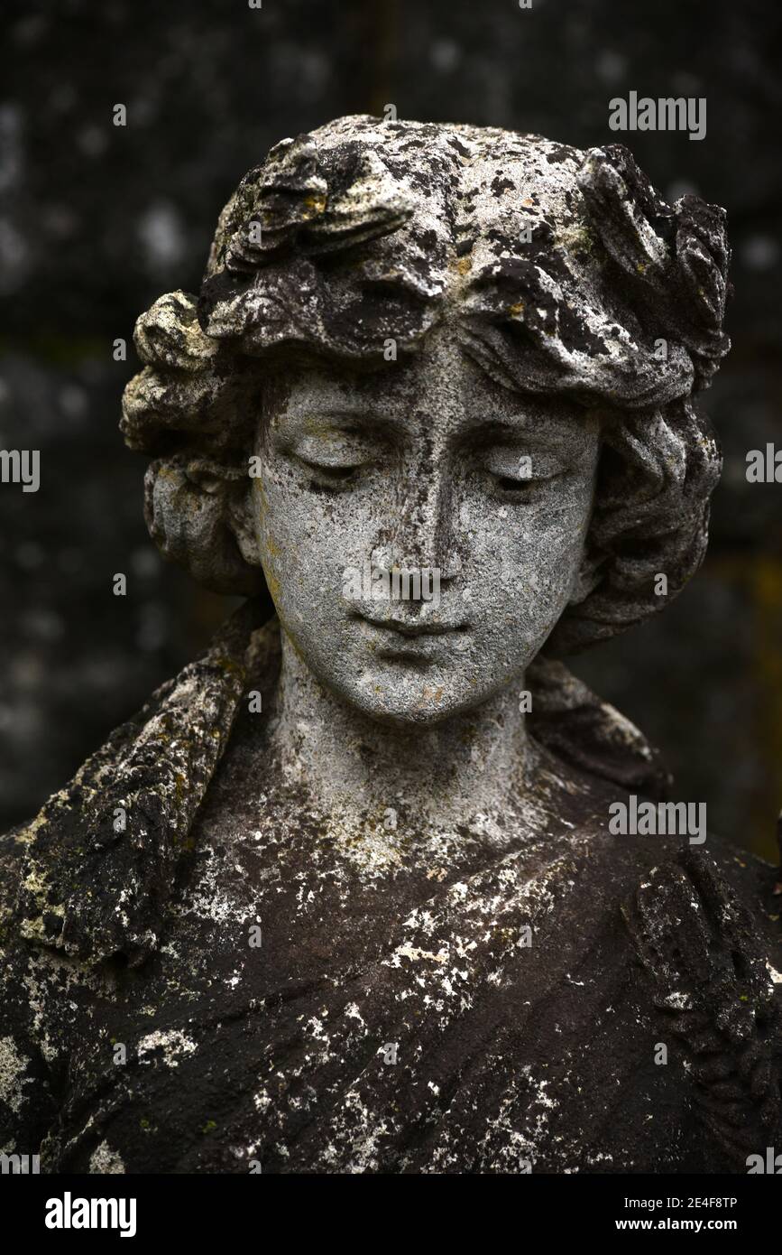 An old stained and lichen covered statue of a young woman with her eyes