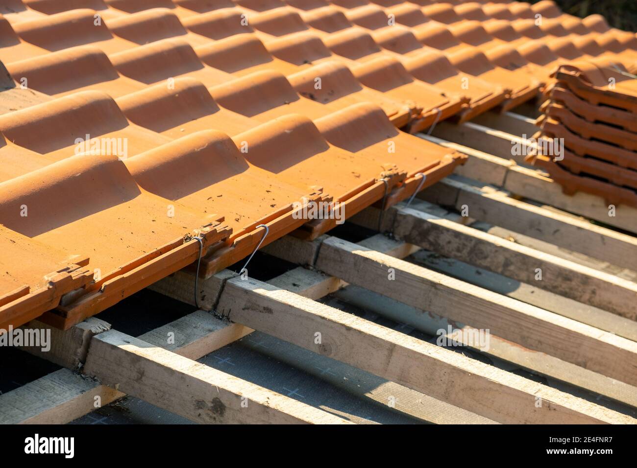 Overlapping rows of yellow ceramic roofing tiles mounted on wooden boards covering residential building roof under construction. Stock Photo