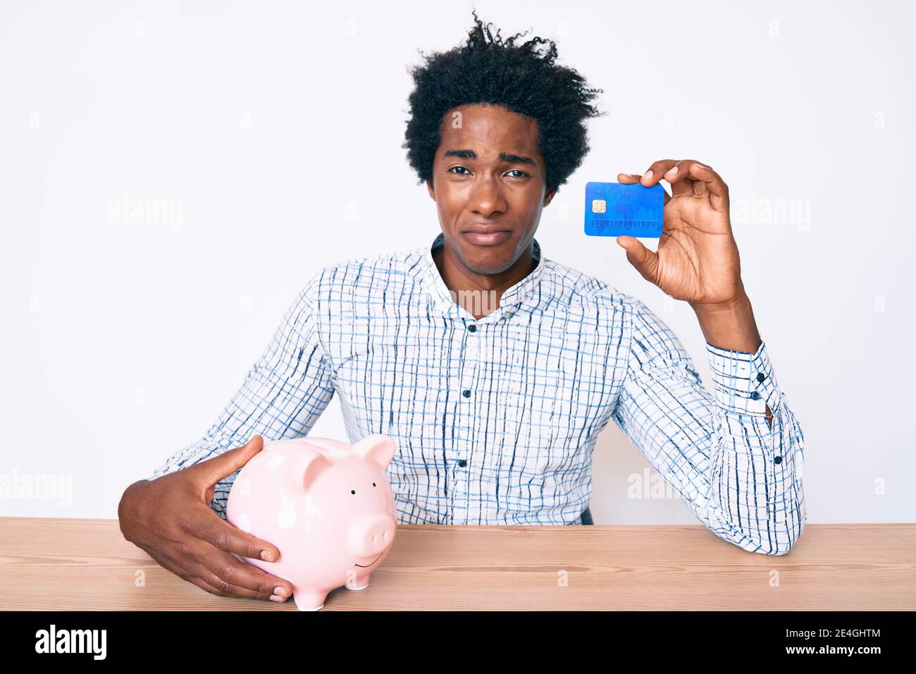 Handsome african american man with afro hair holding credit card and piggy bank depressed and worry for distress, crying angry and afraid. sad express Stock Photo
