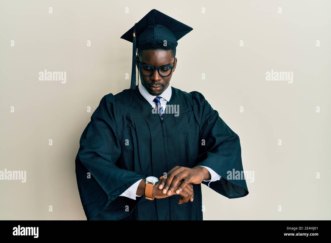 Handsome black man wearing graduation cap and ceremony robe checking the  time on wrist watch, relaxed and confident Stock Photo - Alamy