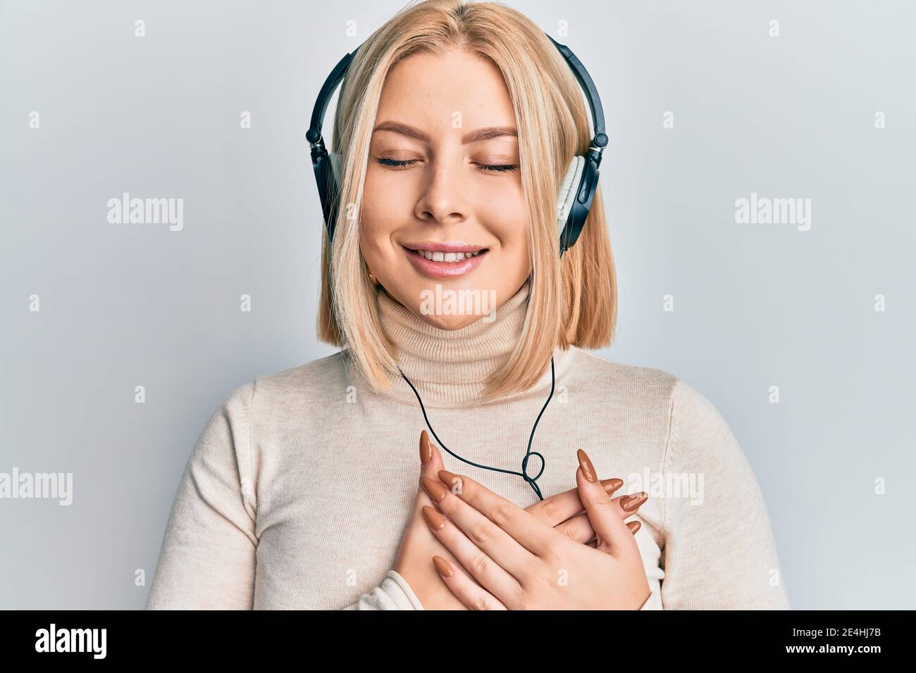 Young blonde woman listening to music using headphones smiling with ...