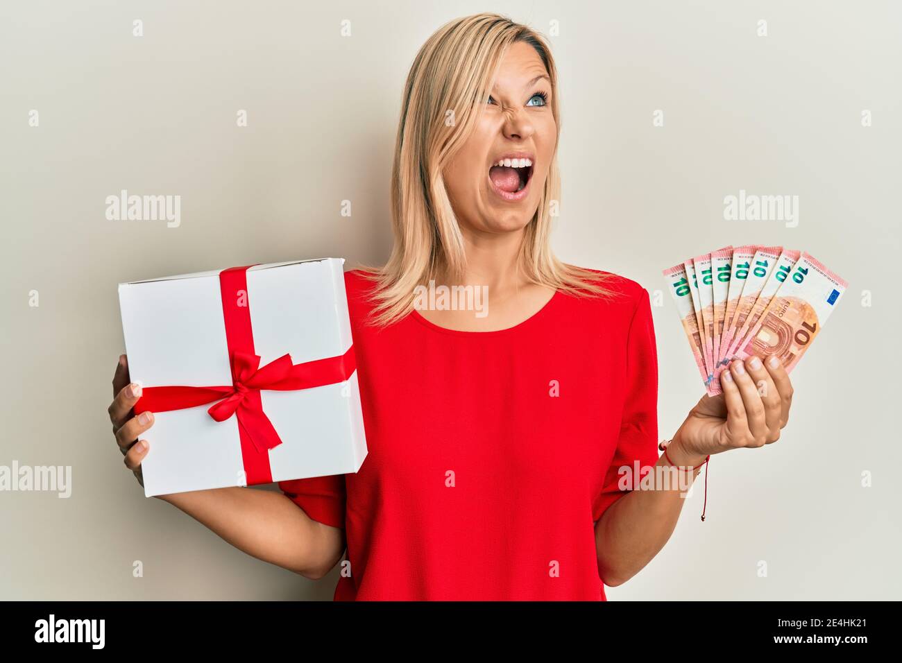 Middle age caucasian woman holding gift and euros banknotes angry and ...