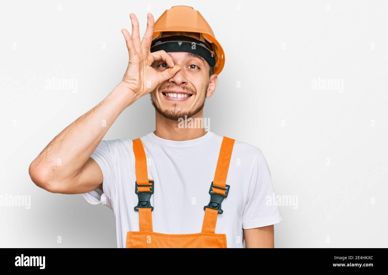 Hispanic young man wearing handyman uniform and safety hardhat smiling ...