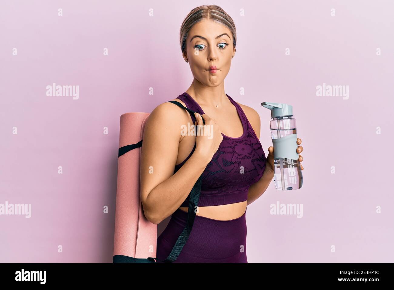 https://c8.alamy.com/comp/2E4HP4C/beautiful-blonde-woman-wearing-sportswear-holding-water-bottle-and-yoga-mat-making-fish-face-with-mouth-and-squinting-eyes-crazy-and-comical-2E4HP4C.jpg