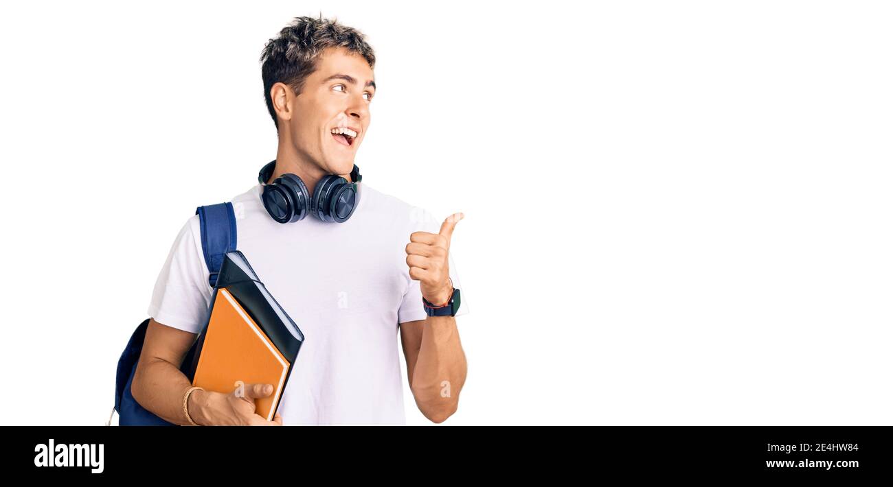 Young handsome man holding student backpack and books pointing thumb up ...