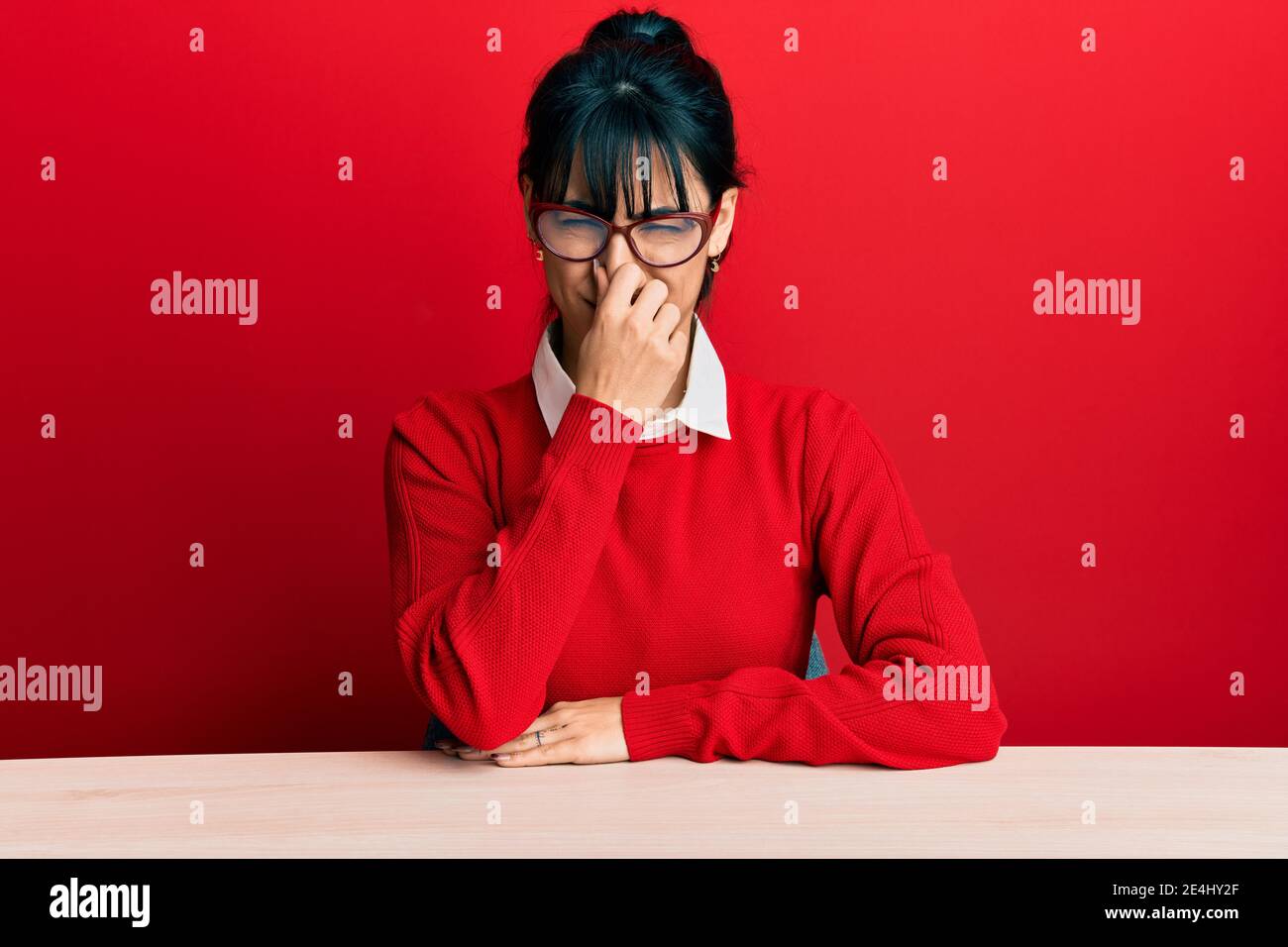 Young Brunette Woman With Bangs Wearing Glasses Sitting On The Table