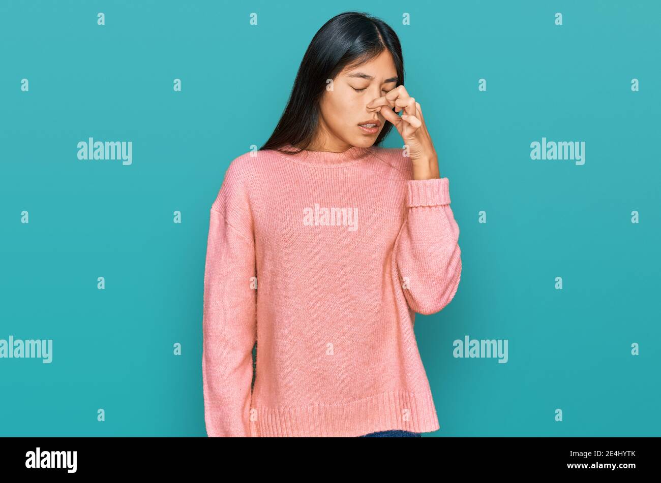 Beautiful young asian woman wearing casual winter sweater smelling something stinky and disgusting, intolerable smell, holding breath with fingers on Stock Photo