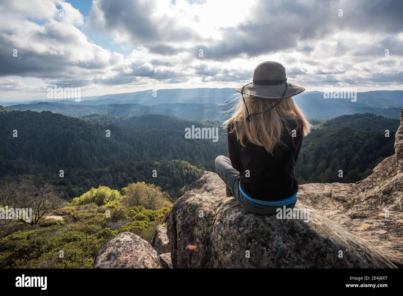A woman sits looking out over the forested hills and wilderness of the Santa Cruz mountains in California. Stock Photo