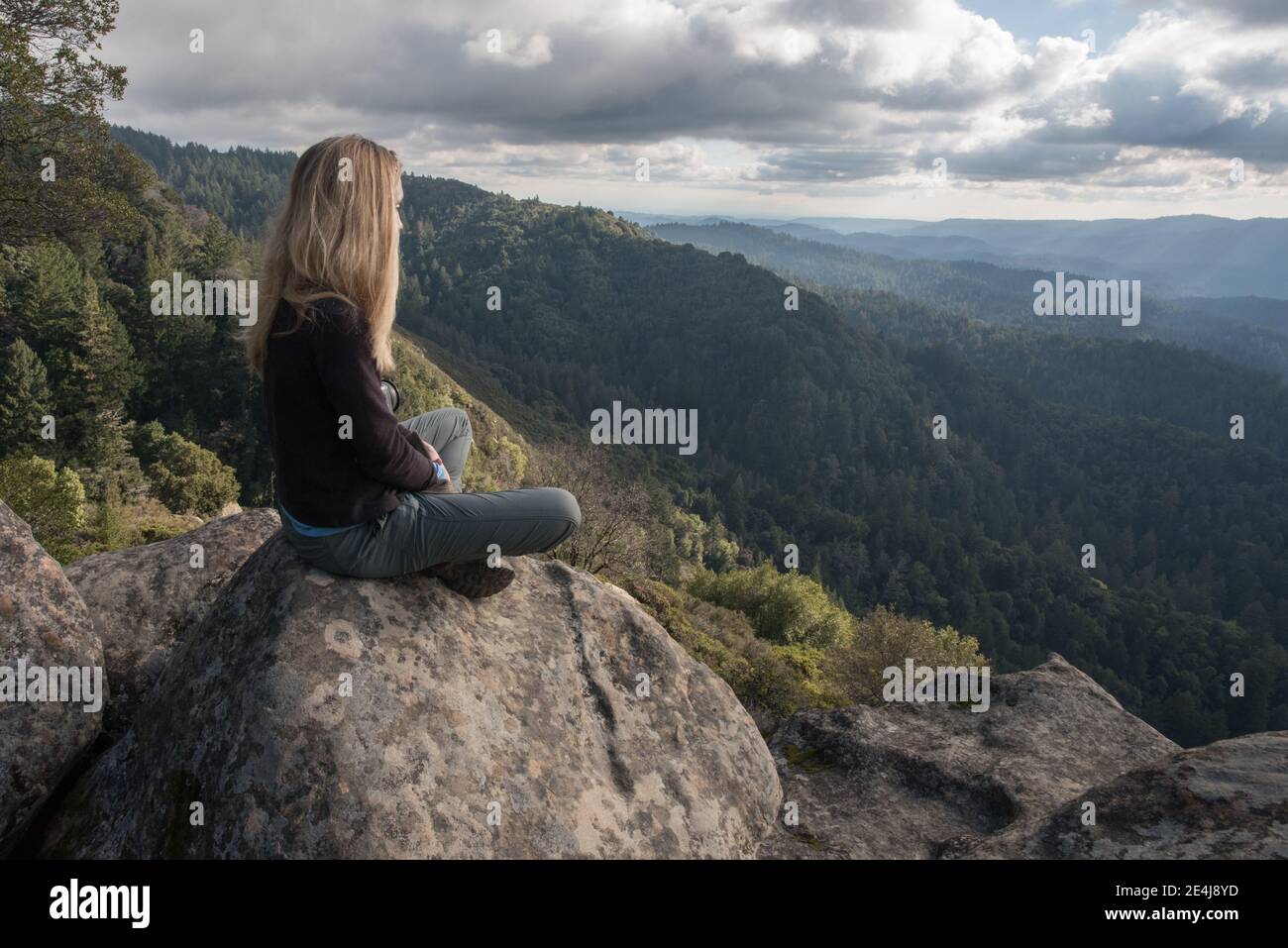 A woman sits looking out over the forested hills and wilderness of the Santa Cruz mountains in California. Stock Photo