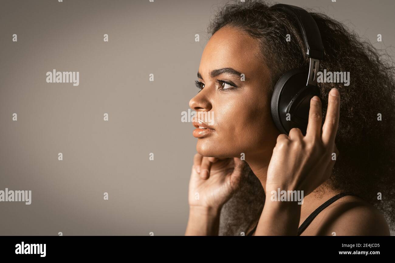 Charming young African-American girl listening her favourite track in headphones wearing red jacket black top under isolated on grey background Stock Photo