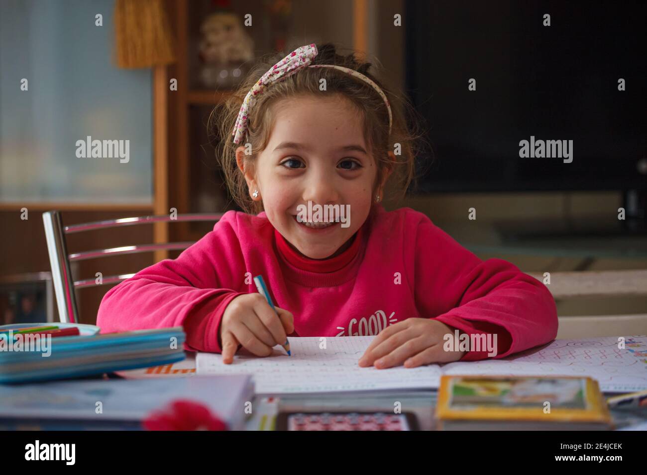 Smiling 6 year old girl does her homework, on the table the case with