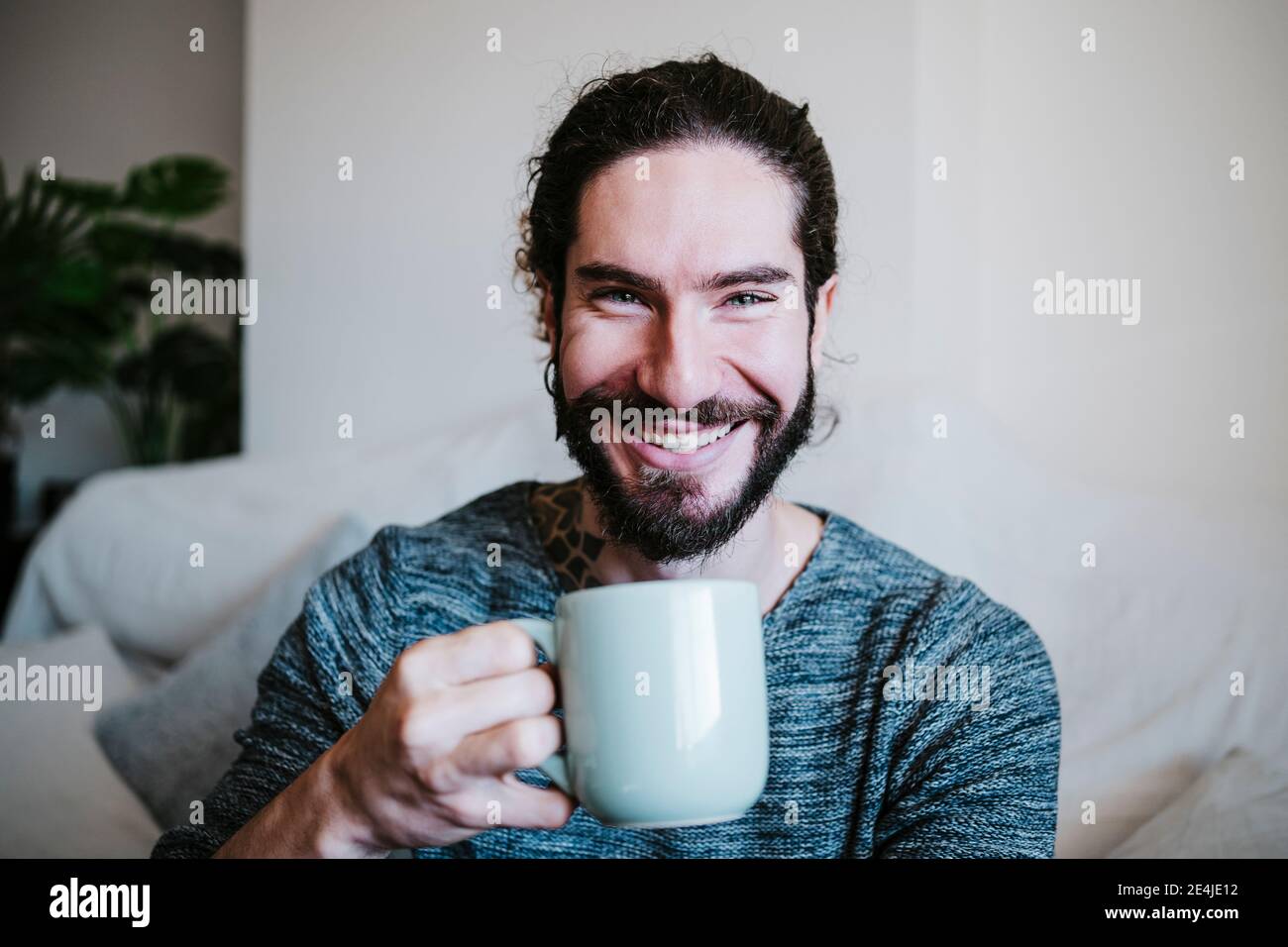 Young man smiling while drinking coffee sitting at home Stock Photo