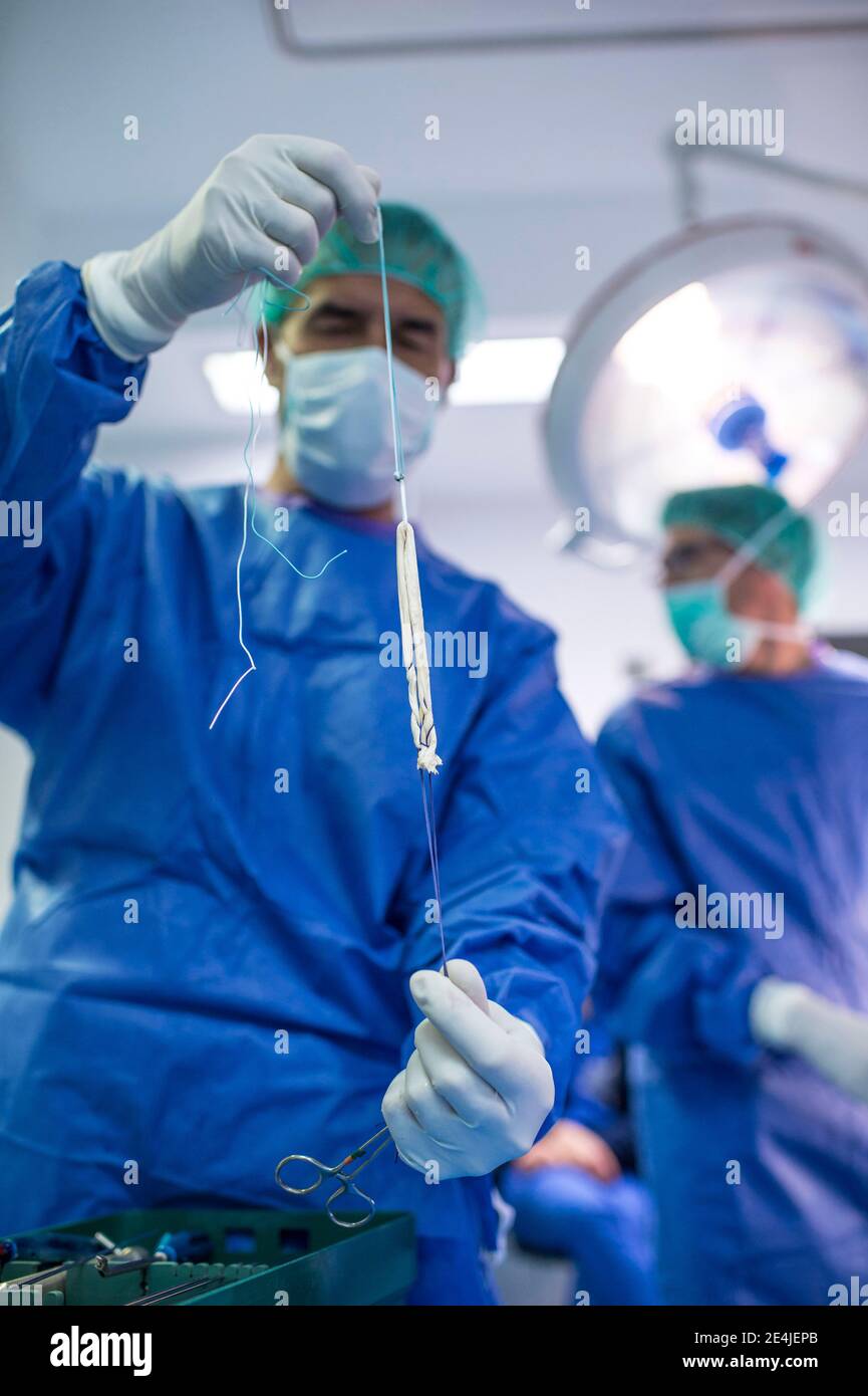 Male orthopedic surgeon preparing knee tendon in operating room Stock Photo