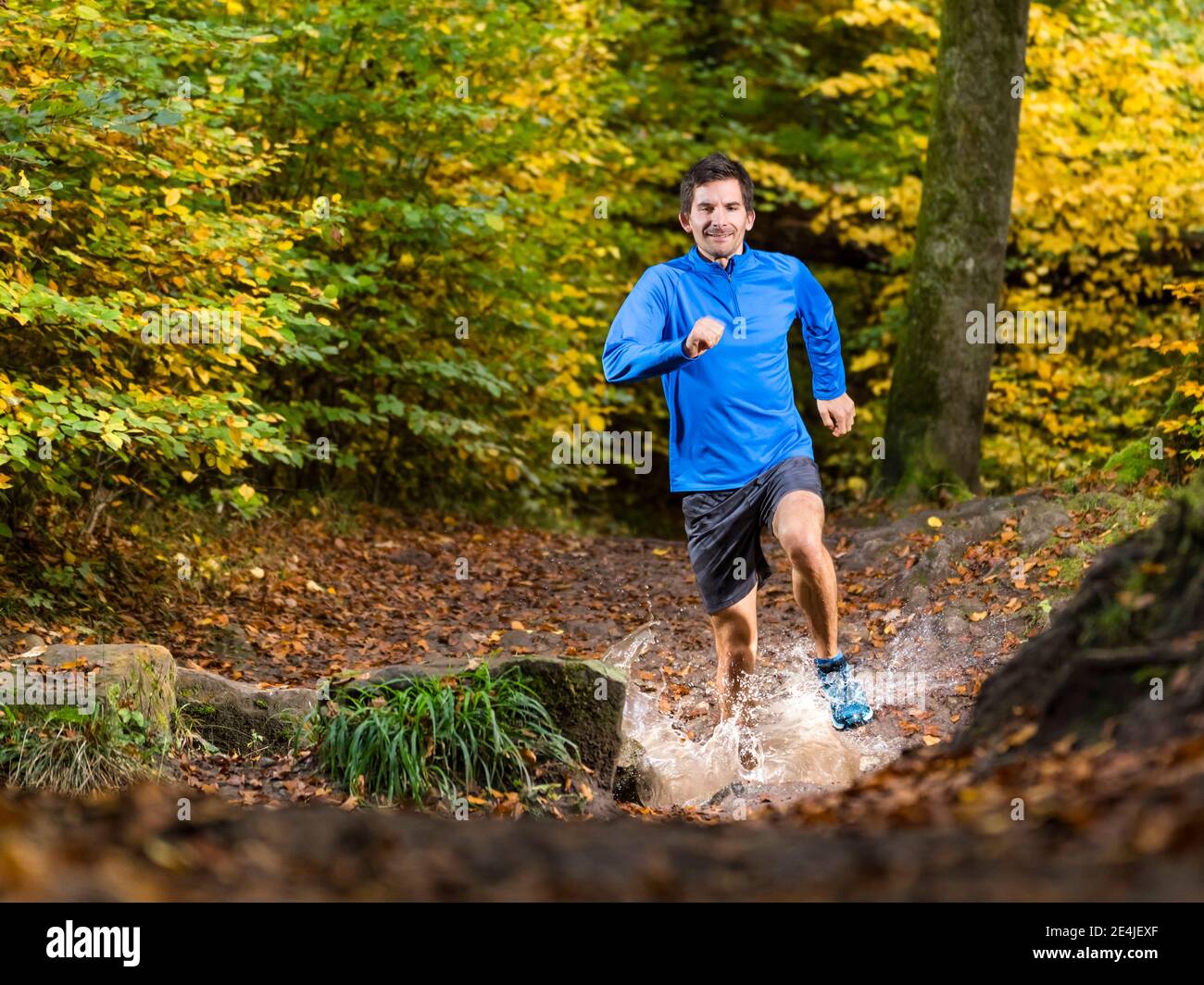 Smiling male sportsperson trail running while splashing water from stream at Kappelberg, Germany Stock Photo