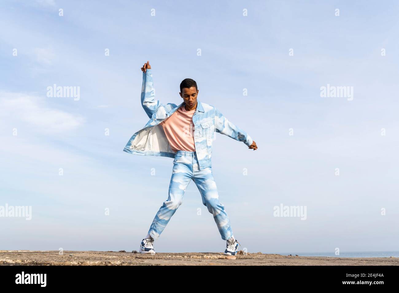 Man wearing denim suit dancing while standing against sky Stock Photo