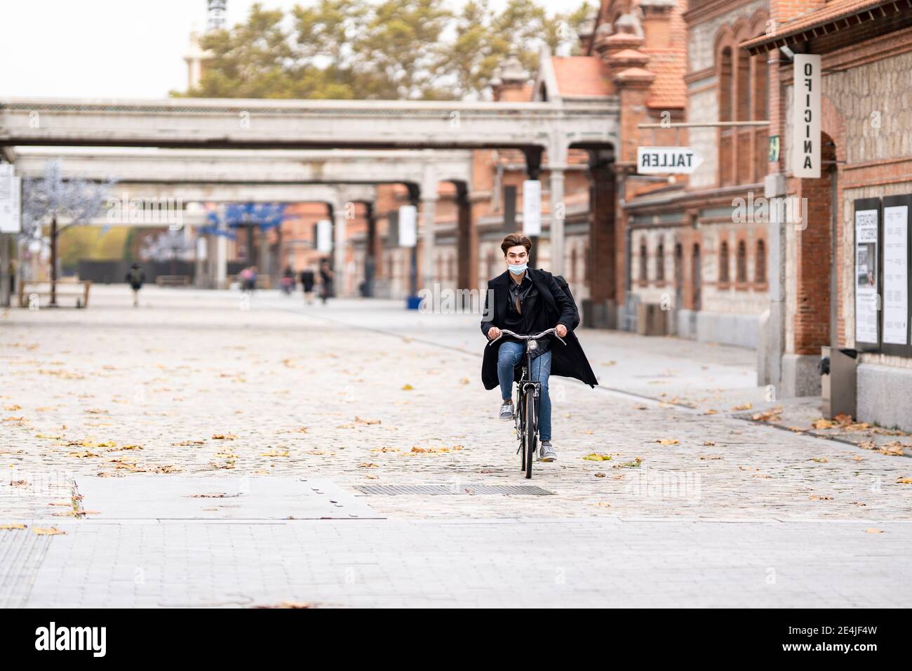 Young man cycling on street with autumn leaves in city during pandemic Stock Photo