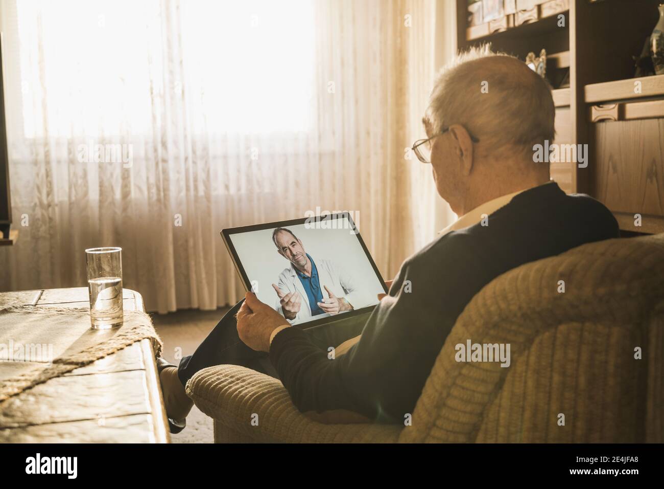 Senior man taking advice from male doctor on video call while sitting on sofa at home Stock Photo