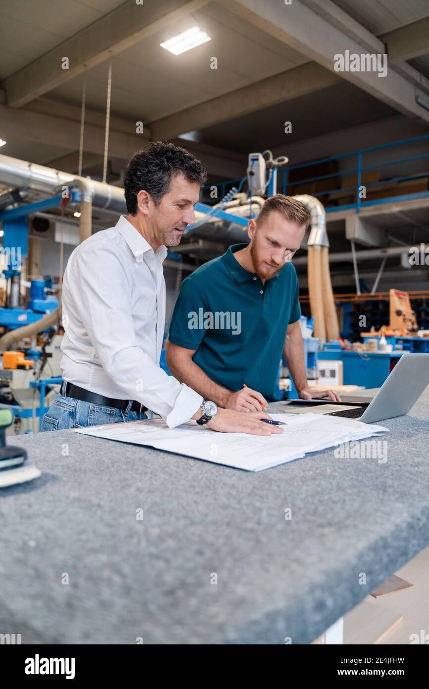Two carpenters talking over documents in production hall Stock Photo