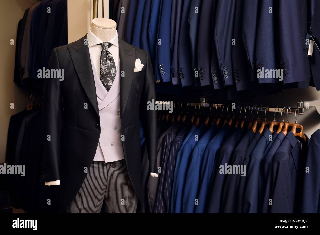 Tailcoat with formal striped trousers on mannequin and blazers on rack in tailors boutique Stock Photo