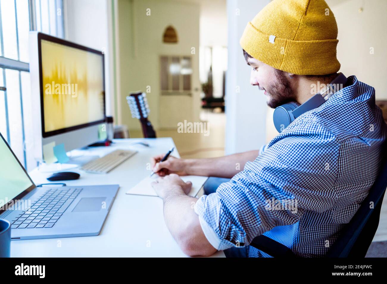 Composer wearing knit hat writing while working at studio Stock Photo